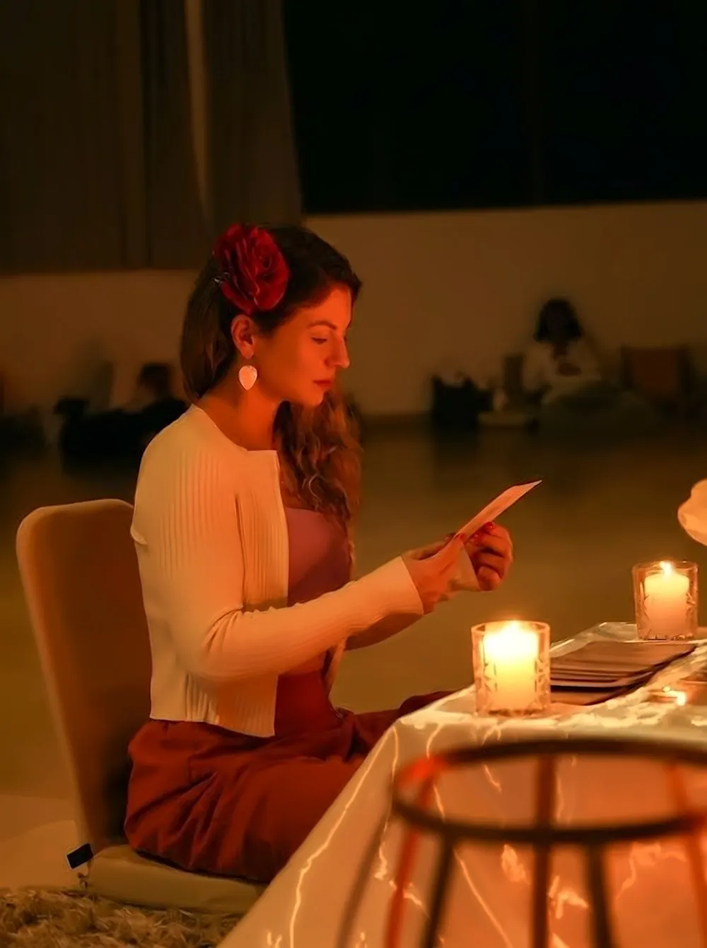 Anna Kuhsler lendo uma carta à luz de velas, com uma flor vermelha no cabelo