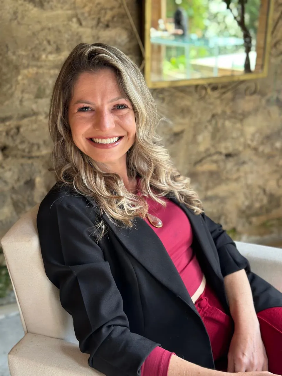Anna Kuhsler sorrindo em uma poltrona clara diante de uma parede de pedra